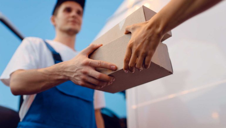 Deliveryman in uniform gives parcel to female recipient at the car, delivery service. Man holding cardboard package near the vehicle, male deliver and woman, courier or shipping job