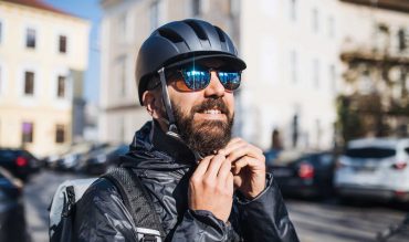 Male hipster courier putting on a helmet in city, delivering packages. Copy space.