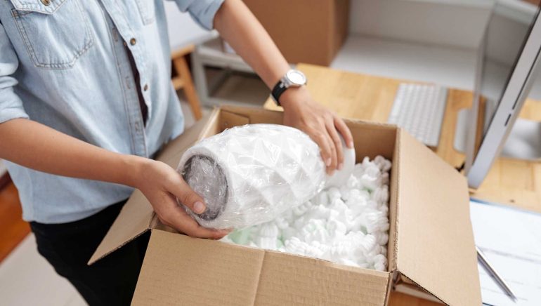 Post office worker packing vase in box for delivery