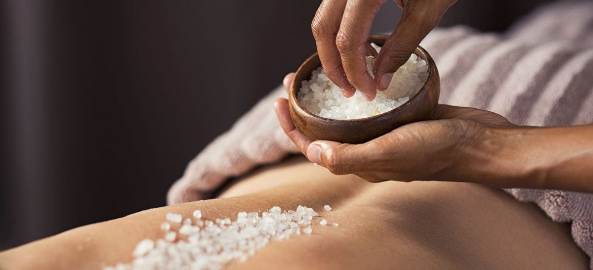 Masseuse hands doing massage on woman's back at beauty salon. Beauty therapist pouring salt scrub on woman back at health spa. Scrubbing and skin care concept.