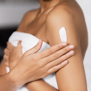 Afro-american girl's hand applying cream on her shoulder. Collagen body butter concept