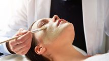 Unrecognizable male beautician putting mask on female face lying with eyes closed with brush in salon.