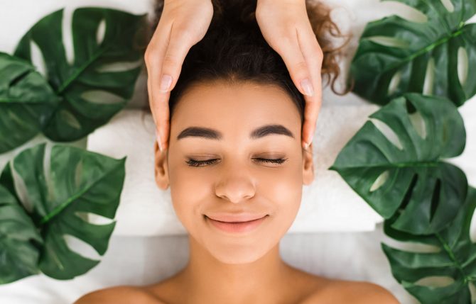 Head massage. Afro girl getting spa treatment with tropical leaves around, top view