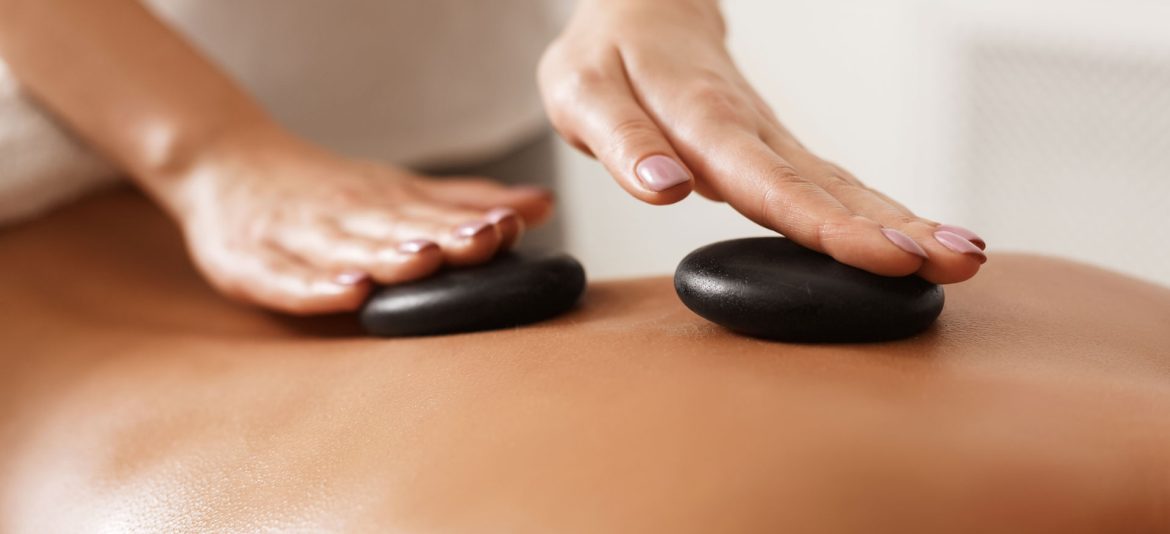 Masseur doing back hot stone massage to woman in spa salon, closeup