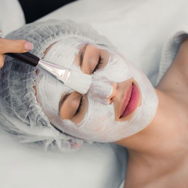 Portrait of young woman while facial cosmetic procedure in spa salon.