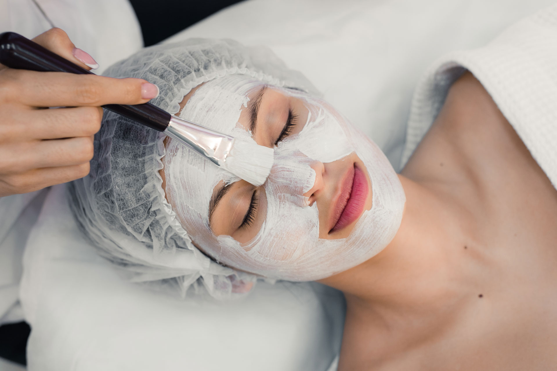 Portrait of young woman while facial cosmetic procedure in spa salon.